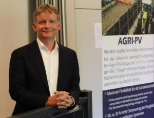 Porträtaufnahme von Dr. Gunter Erfurt, dem neuen Aufsichtsratsvorsitzenden der Next2Sun AG, im dunklen Anzug vor einem Informationsbanner zur Agri-Photovoltaik